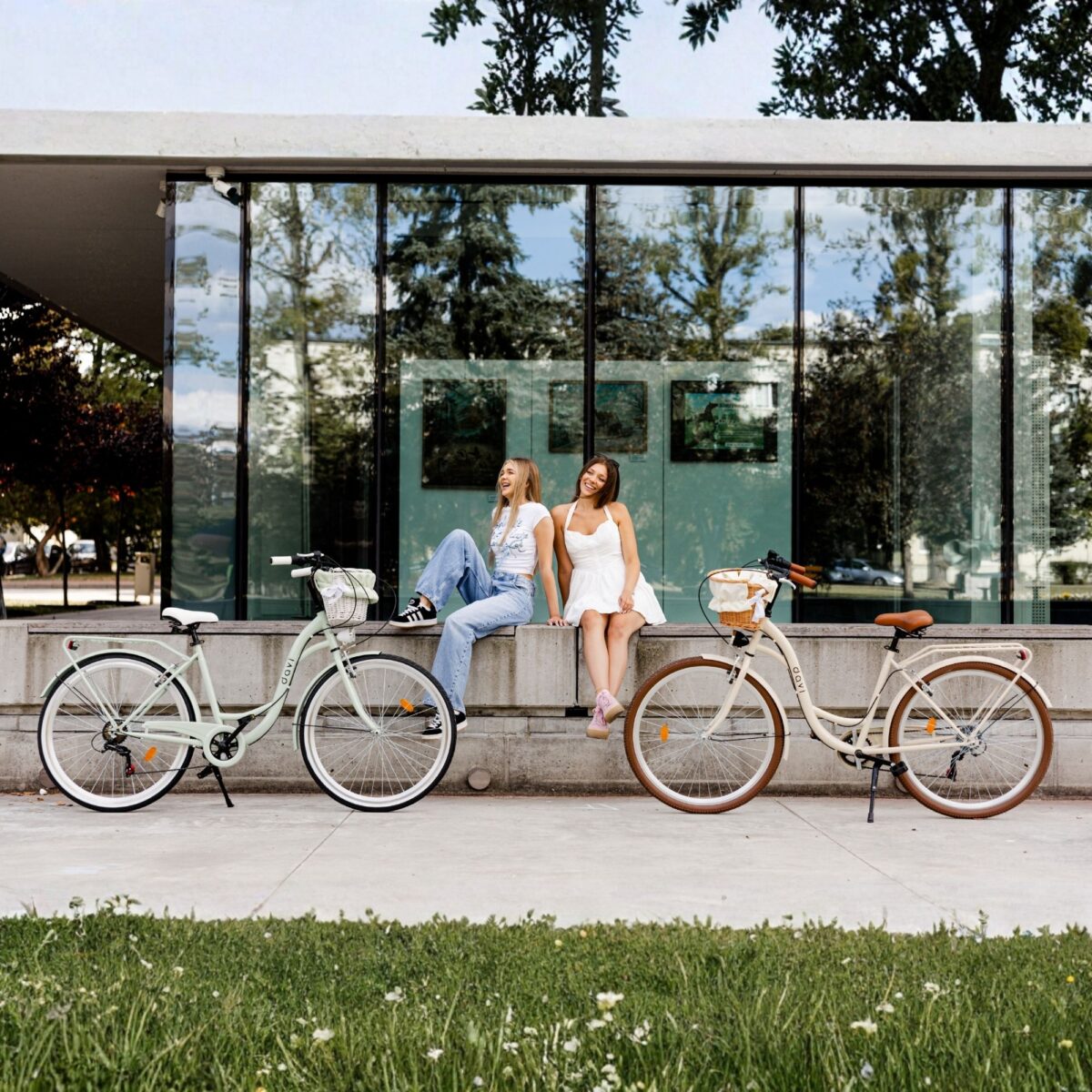 Dvoje ljudi sjedi pored bicikala ispred zgrade.