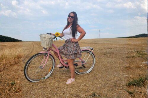 Žena s biciklom u polju sa suncokretom.