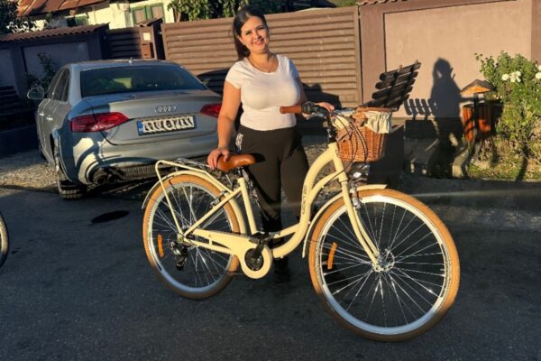 Žena s biciklom ispred automobila u dvorištu.